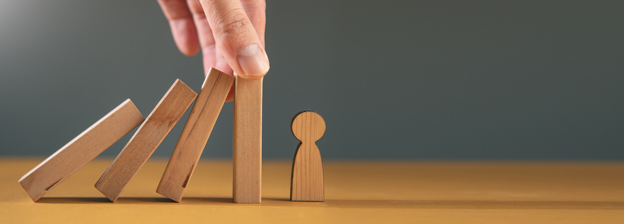 Wooden domino pieces being knocked down toward a human shaped piece