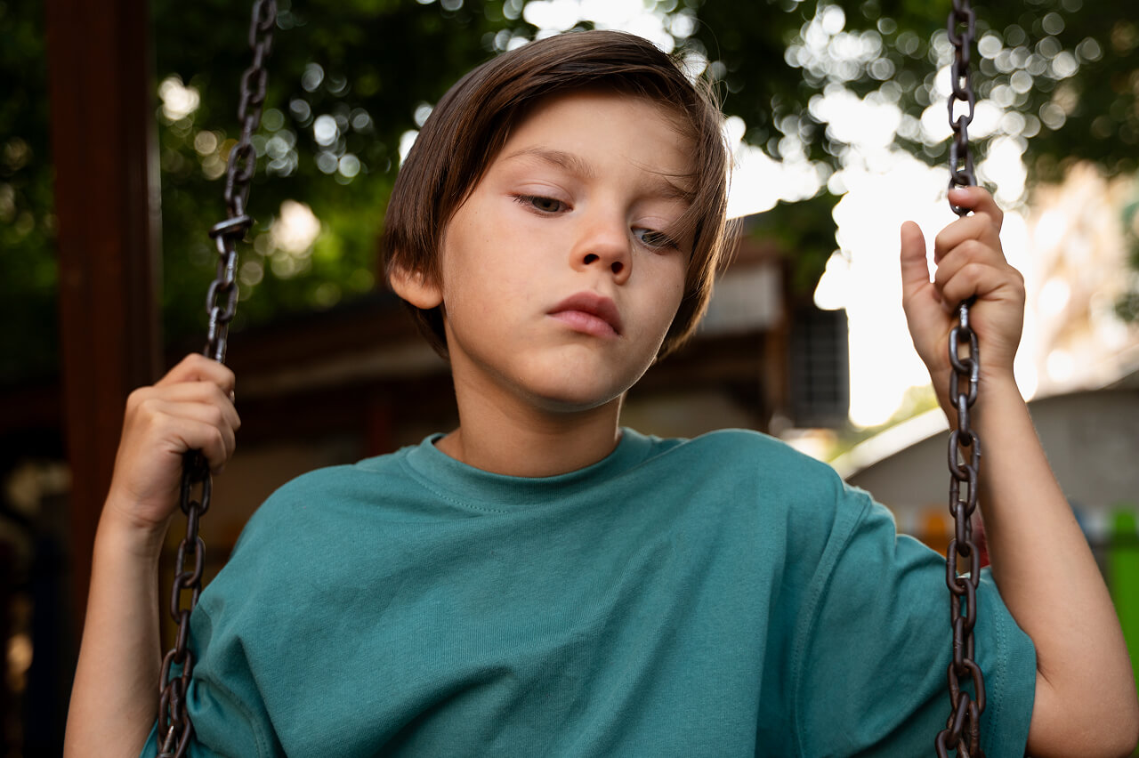 Front view of a young child sitting on a swing with a sad look