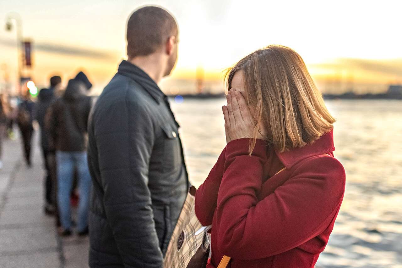 A couple stand in the sunset, the woman cradles her head with her hands.
